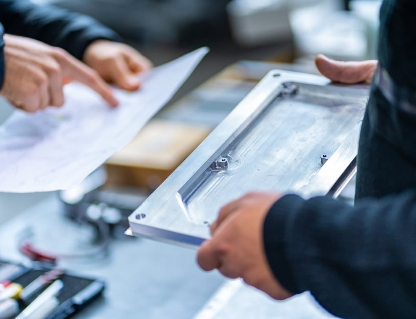 Engineers examine a milled component and review an engineering drawing