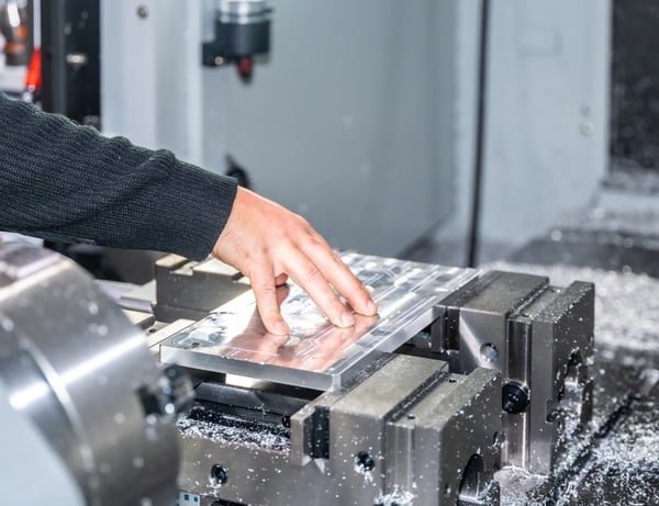 A machinist loads an aluminum plate into a 3-axis mill